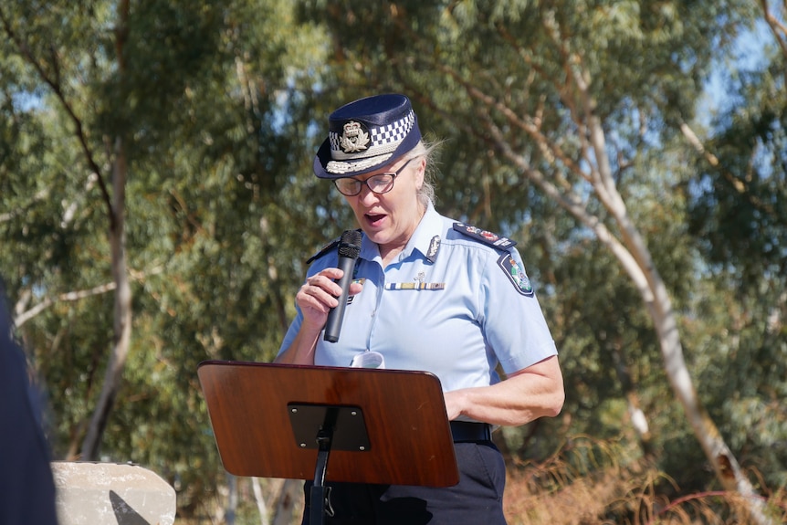 A female police officer speaks outdoors, holding a microphone.