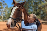 Women in her 80s pictured up close patting a chestnut horse with its eyes closed. 