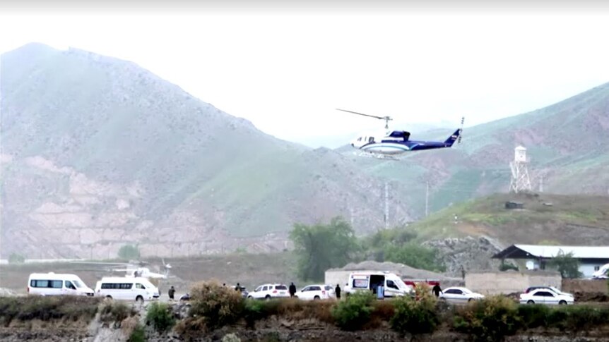 A blue and white helicopter takes off in front of mountains in heavy fog. 