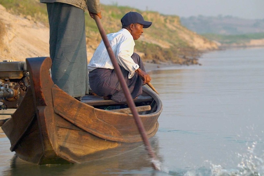 U Maung Lay crouches in his boat looking into the water