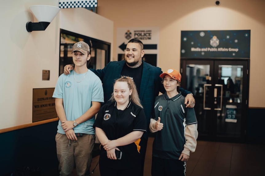 Man standing with arms around a group of three kids smiling for as photo