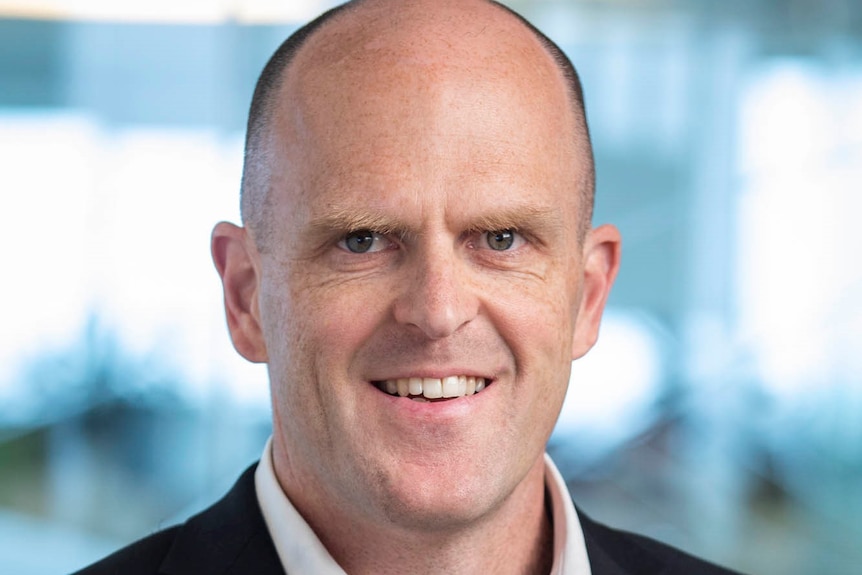 Head shot of man with a shaved head wearing a shirt and charcoal jacket