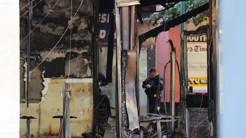 A police officer in the ruins of a burnt out restaurant.