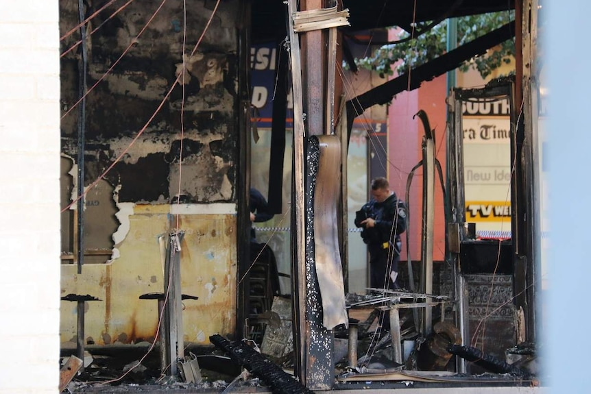 A police officer in the ruins of a burnt out restaurant.