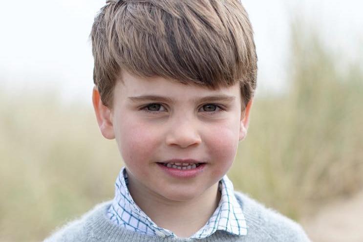 A portrait photograph of Prince Louis wearing a grey jumper.