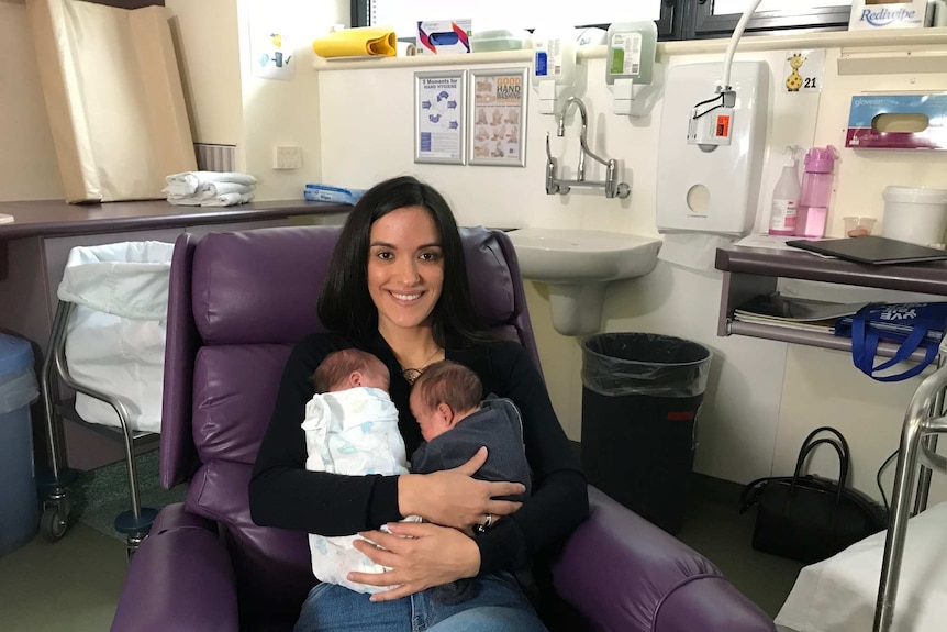 A woman sitting down and holding two babies.