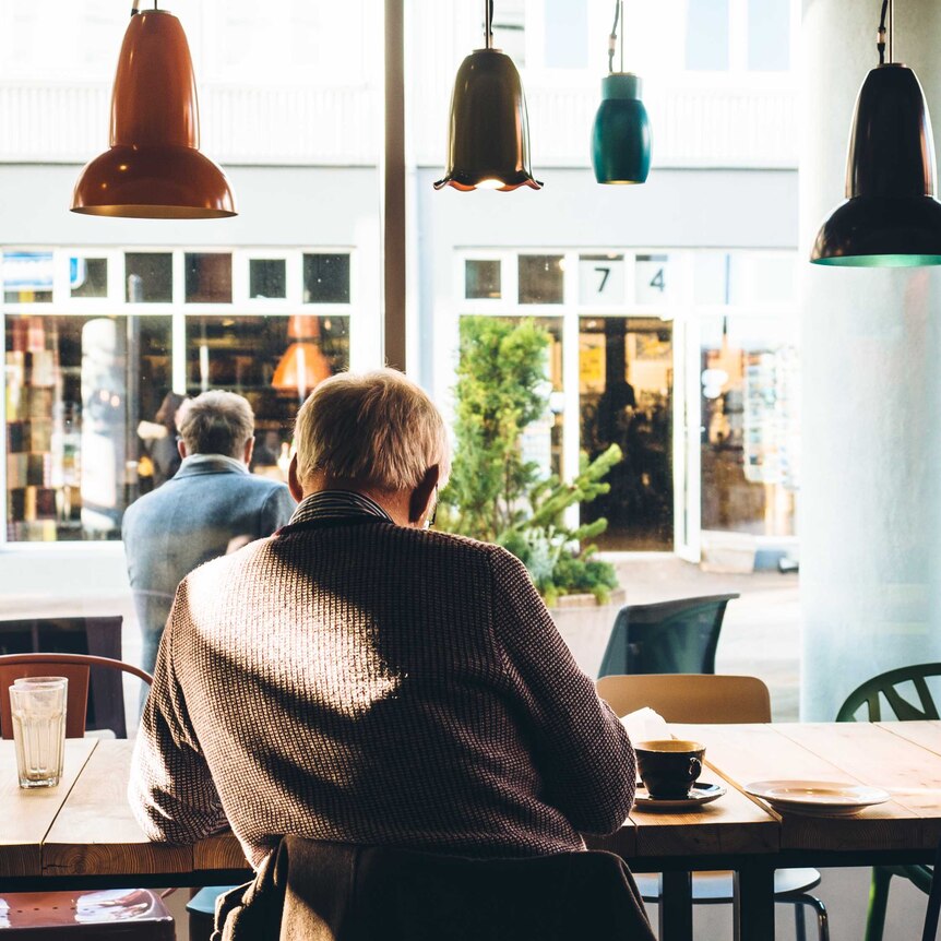 An older man sits alone in cafe reading the paper and drinking coffee.