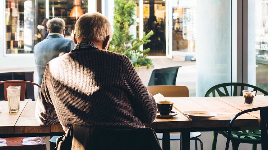 An older man sits alone in cafe reading the paper and drinking coffee.