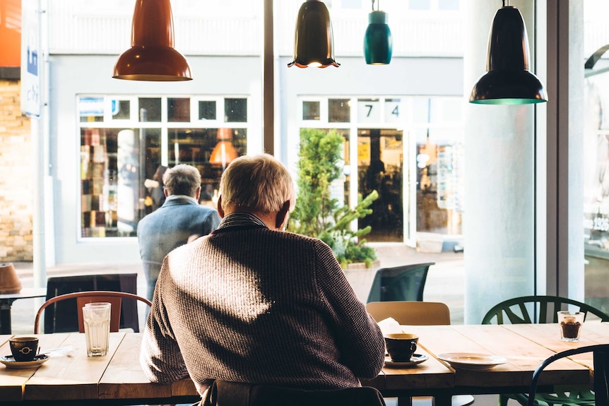 An older man sits alone in cafe reading the paper and drinking coffee.