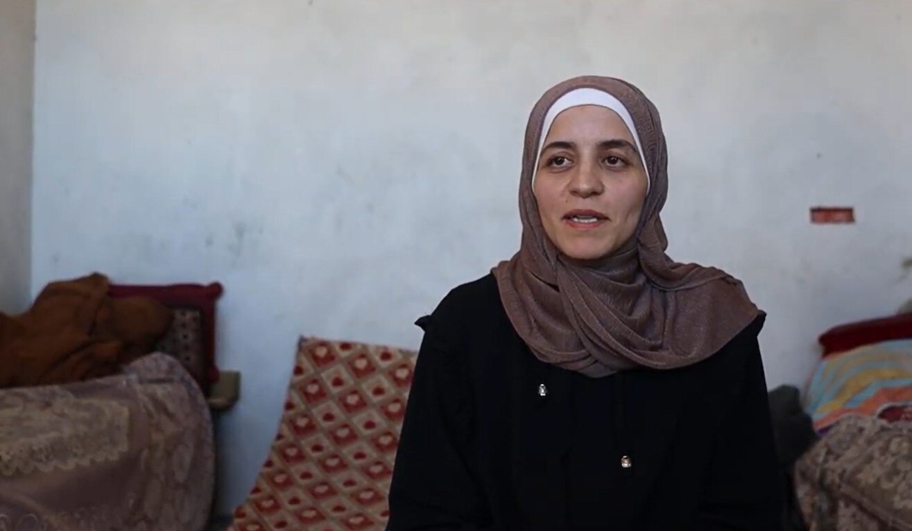 Mervat Sarhan, dressed in traditional Palestinian clothes, sits and talks on a cushion.