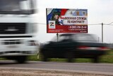 cars drive by an army recruitment billboard reading "Contract military service" and showing a soldier in uniform