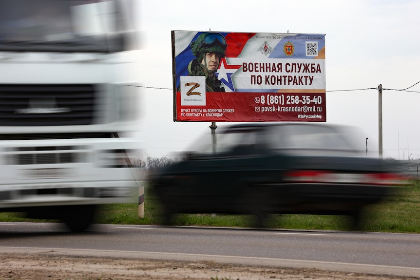 cars drive by an army recruitment billboard reading "Contract military service" and showing a soldier in uniform