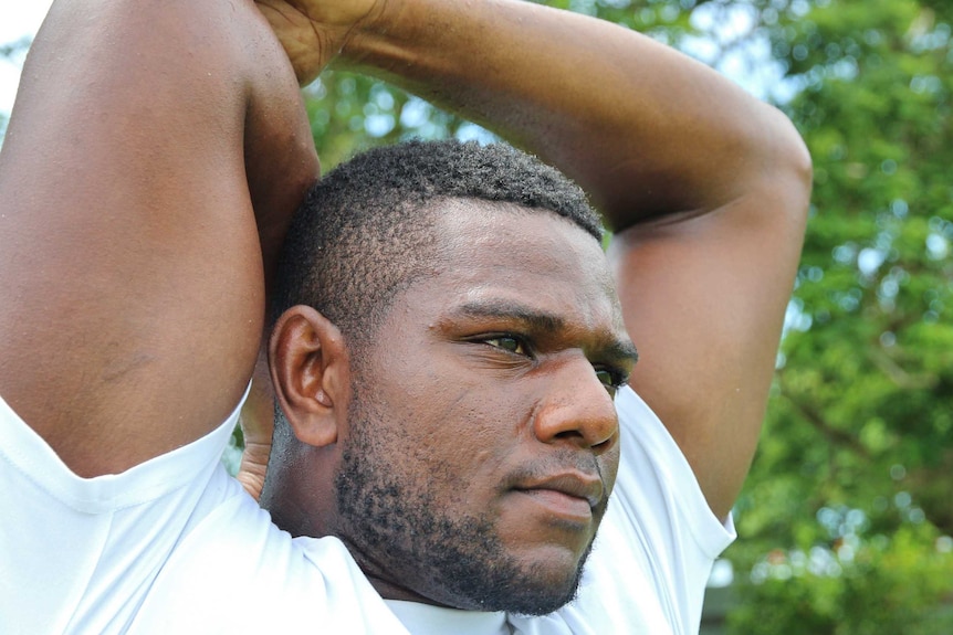 Mustafa puts his arms behind his head to stretch his triceps.