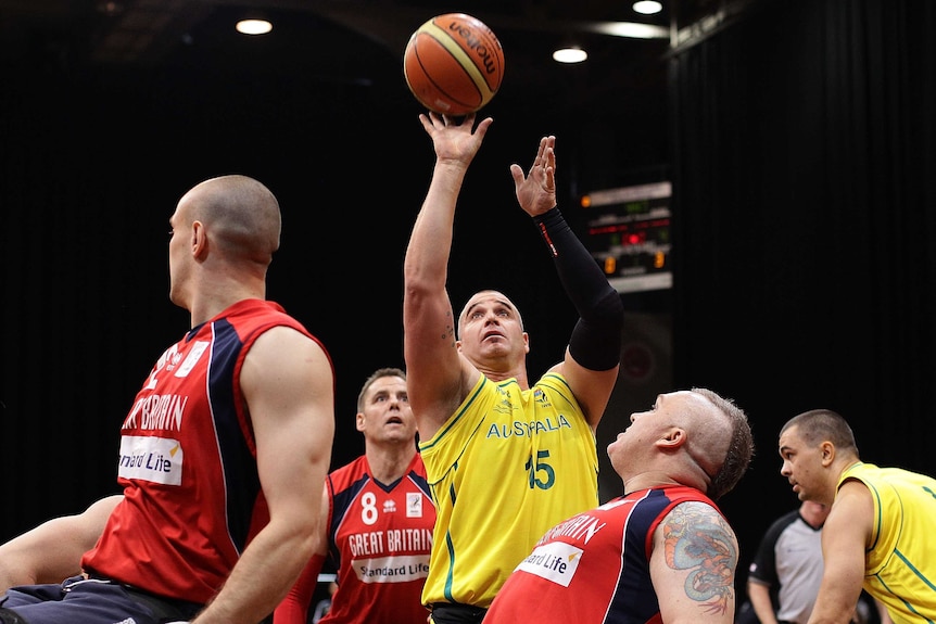 A man shoots a basketball into the air while four other players watch during a game of wheelchair basketball.