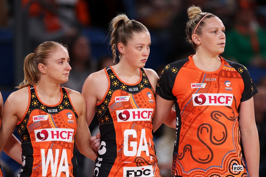 Harten stands arm in arm with her Giants teammates, wearing a training top over her dress