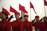 Wide shot of a line of women in red uniform standing and saluting.