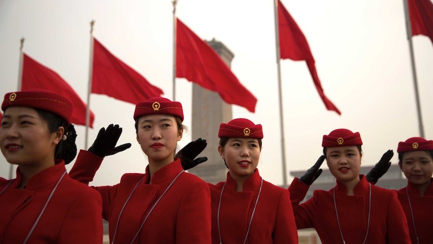 Wide shot of a line of women in red uniform standing and saluting.