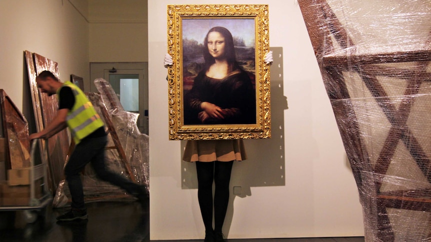 A gallery employee positions a copy of the Mona Lisa.