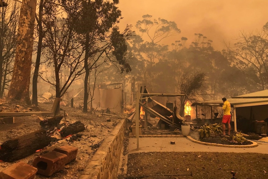 Man in surf lifesaver shirt standing outside a burning house.