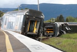 A train carriage lies on its side next to another upright carriage. 