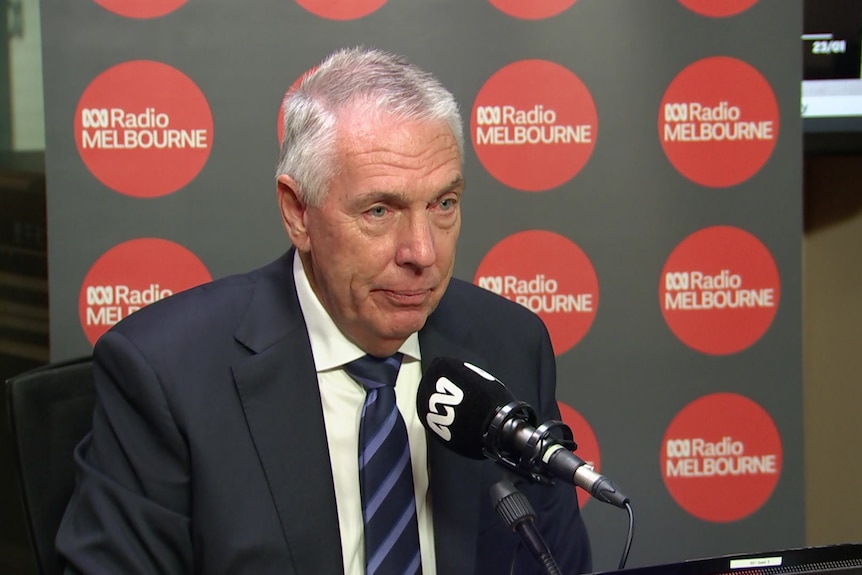 Peter Walsh wears a dark jacket, white collared shirt and blue striped tie and sits in an ABC radio studio.