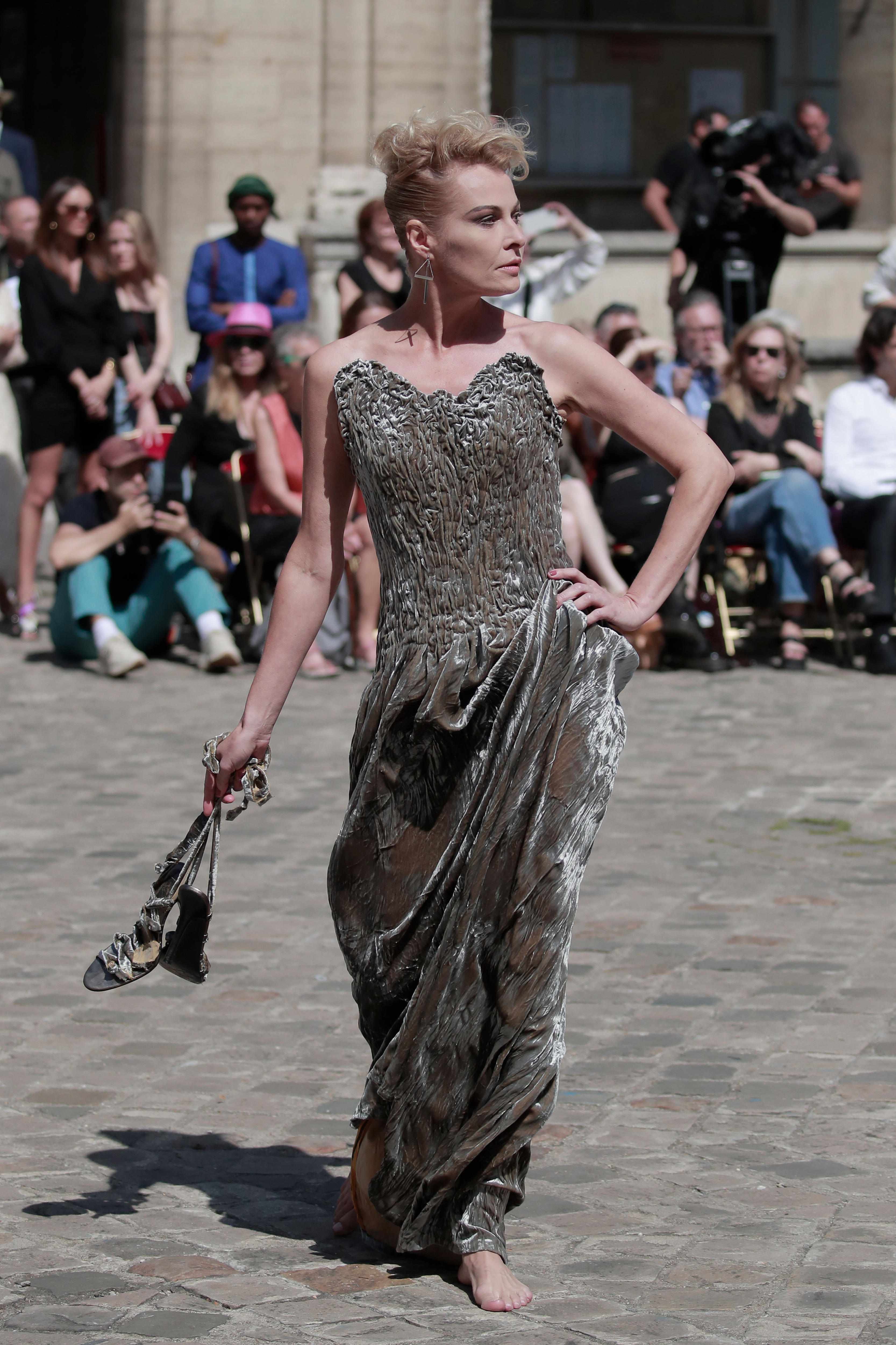 A model in a sparkly dress holding a pair of high heel shoes. 