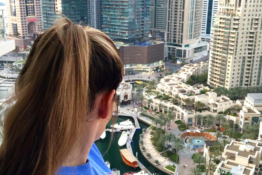 Woman has back to camera overlooks Dubai Marina. 