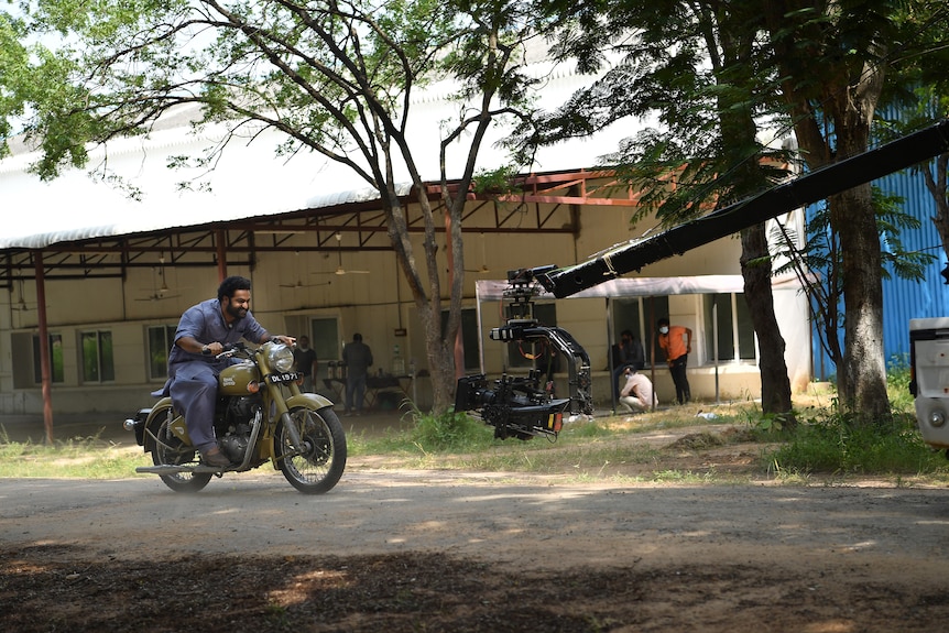 Un homme conduit une moto tout en étant photographié par un appareil photo.