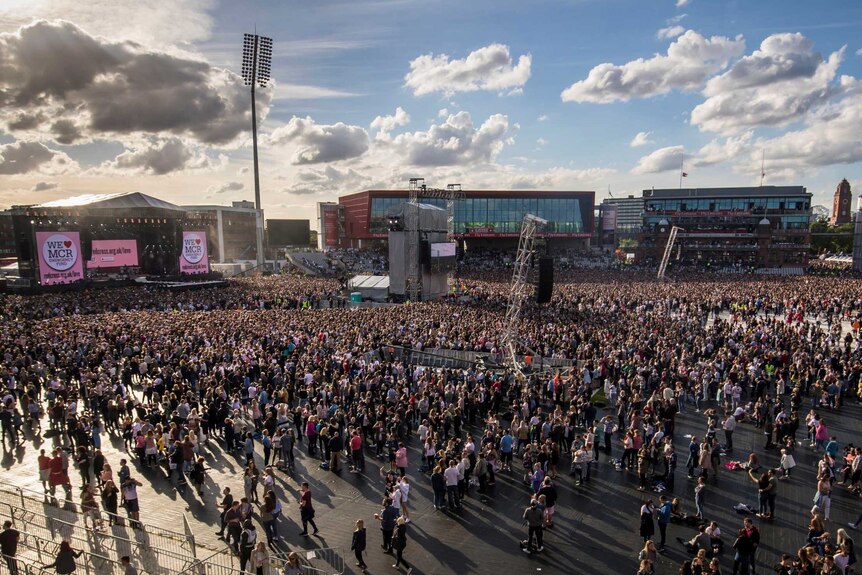 A large crowd waits in front of the stage under plump clouds sitting in a blue sky.