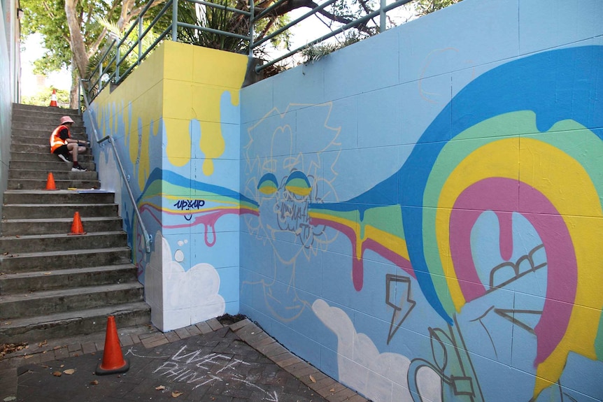 An artist works on a mural that extends all the way up a flight of stairs