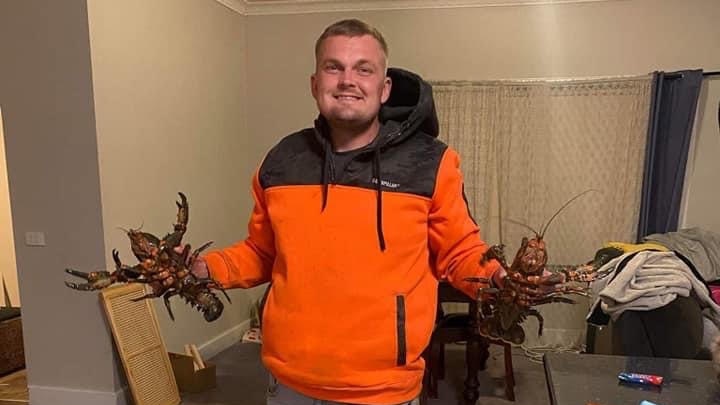 A man in a hi vis jumper holds up two shellfish. He is smiling.