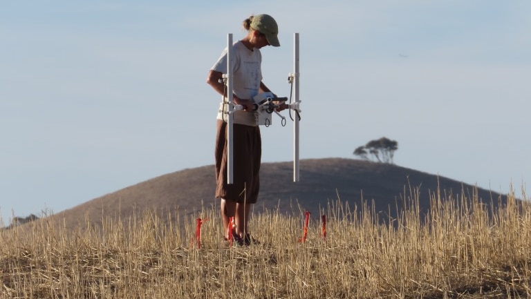 A woman holding a machine in a field with a hill behind