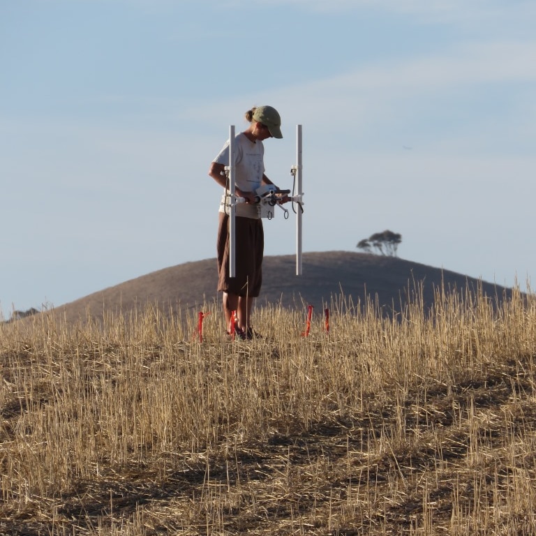A woman holding a machine in a field with a hill behind