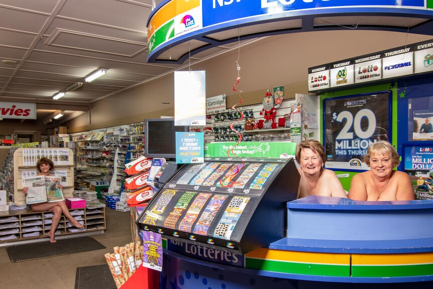 Three women in a newsagent, one is holding a newspaper over her chest.