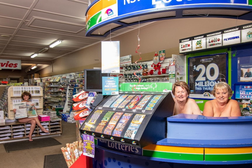 Three women in a newsagent, one is holding a newspaper over her chest.