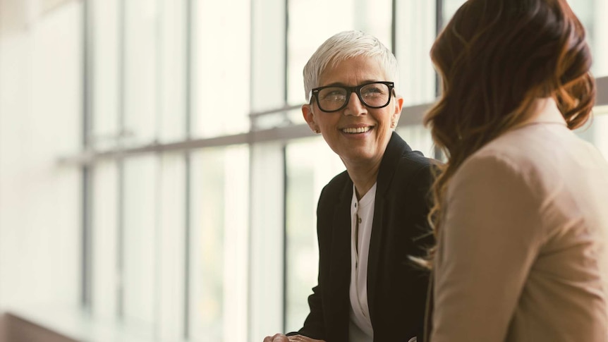 An older office worker talks with a younger woman.