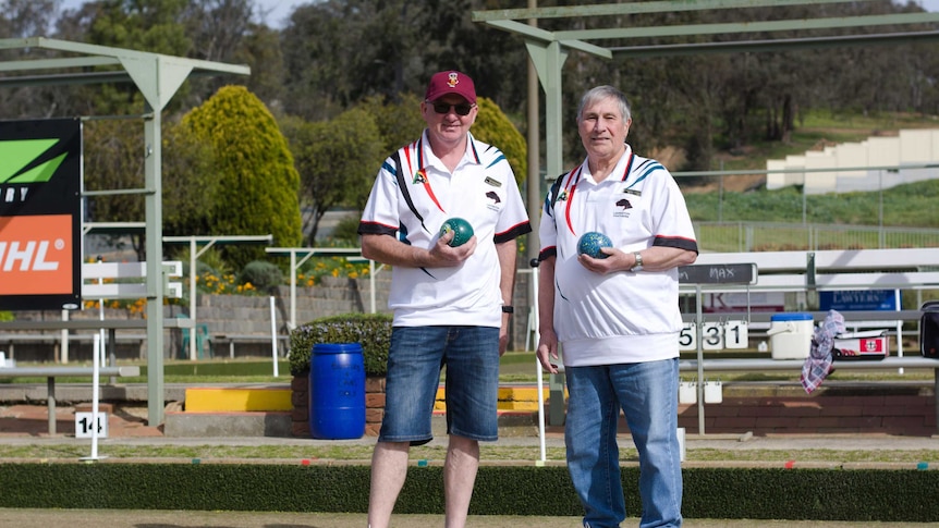 man with cap and glasses stands next to man with grey hair holding lawn bowls balls