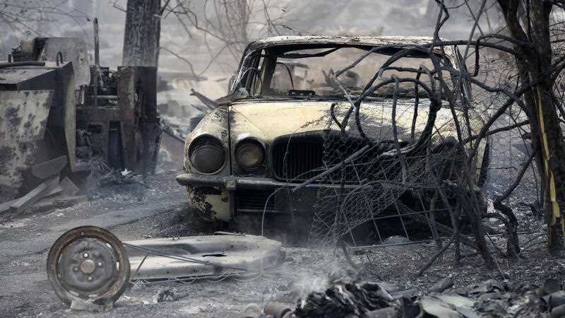 A burnt-out shell of a vehicle in a smoky setting.