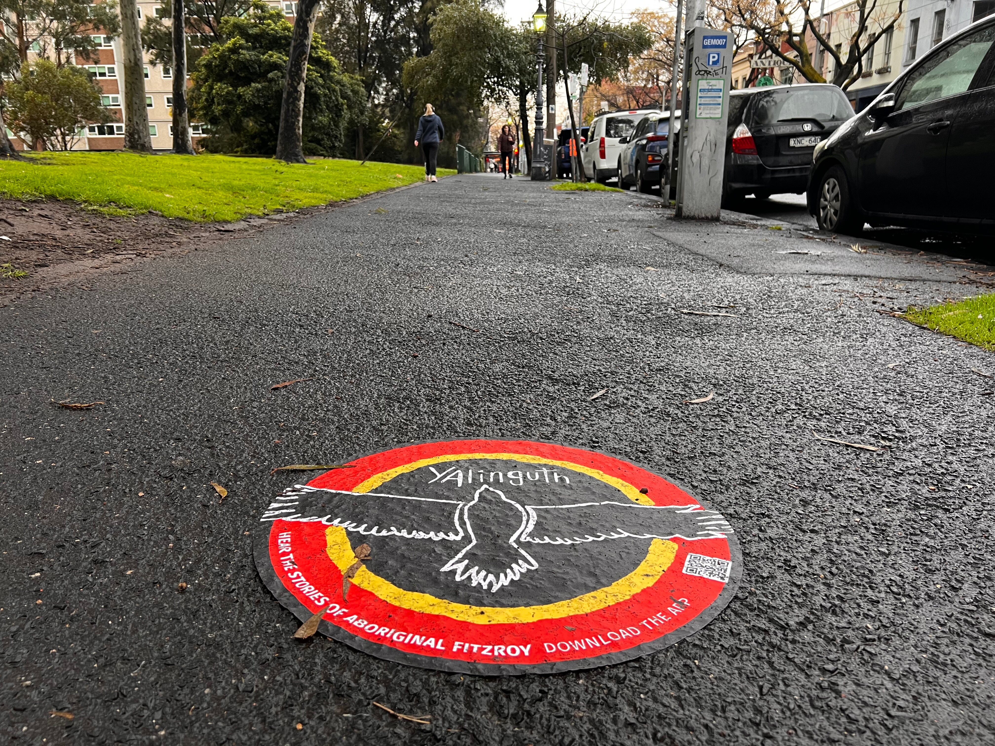 A black, yellow and red sticker with an eagle reads 'Yalinguth', on a wet Melbourne footpath.