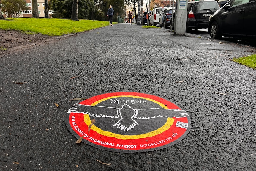 A black, yellow and red sticker with an eagle reads 'Yalinguth', on a wet Melbourne footpath.