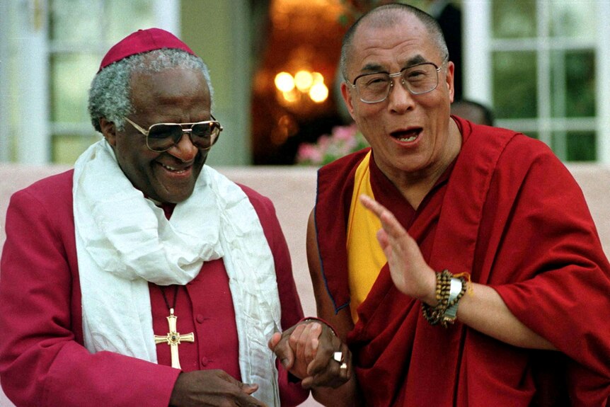Archbishop Desmond Tutu smiles as he shakes the hand of the Dalai Lama, both wearing red