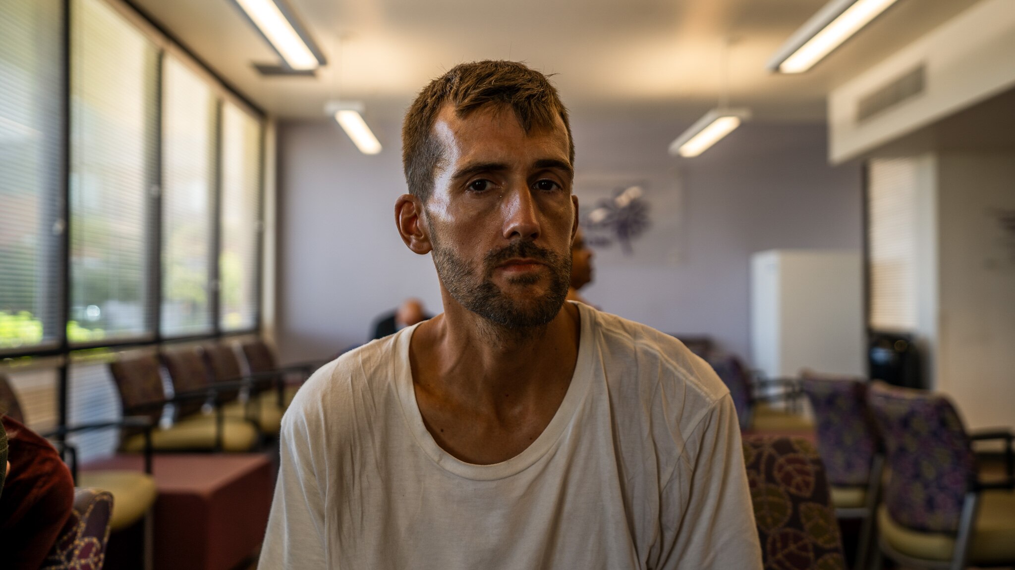 A man with a beard wearing a white shirt sits down in an airconditioned room.