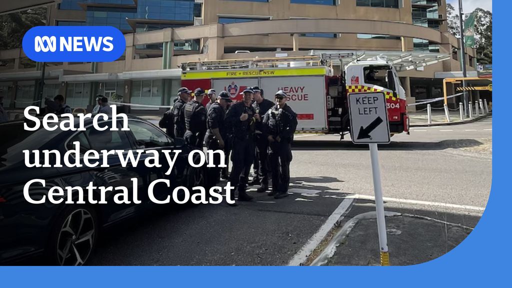 Seach underway on Central Coast: Police in navy uniforms stand around on a street. In the background is a firetruck.