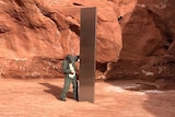 A man inspects the shiny metal object in a red rock canyon