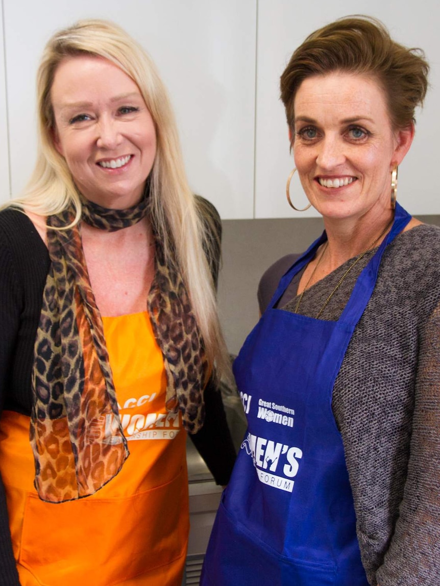 Two women wearing aprons in a kitchen.