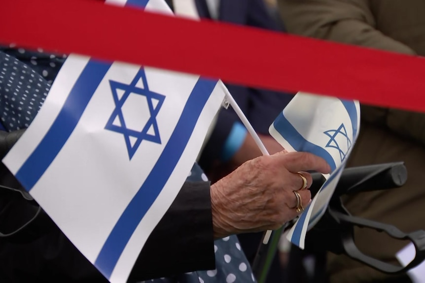 An elderly woman's hands are pictured holding two small Israeli flags