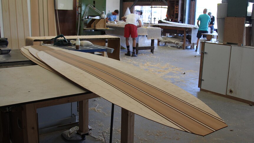 Wooden surfboard skins sitting on a wooden workbench in an industrial workshop.