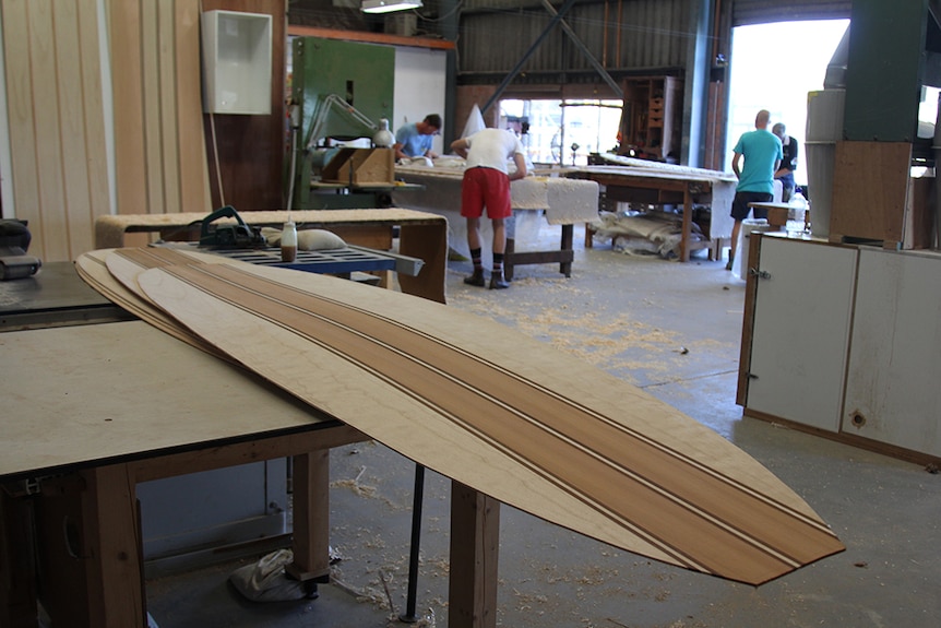 Wooden surfboard skins sitting on a wooden workbench in an industrial workshop.