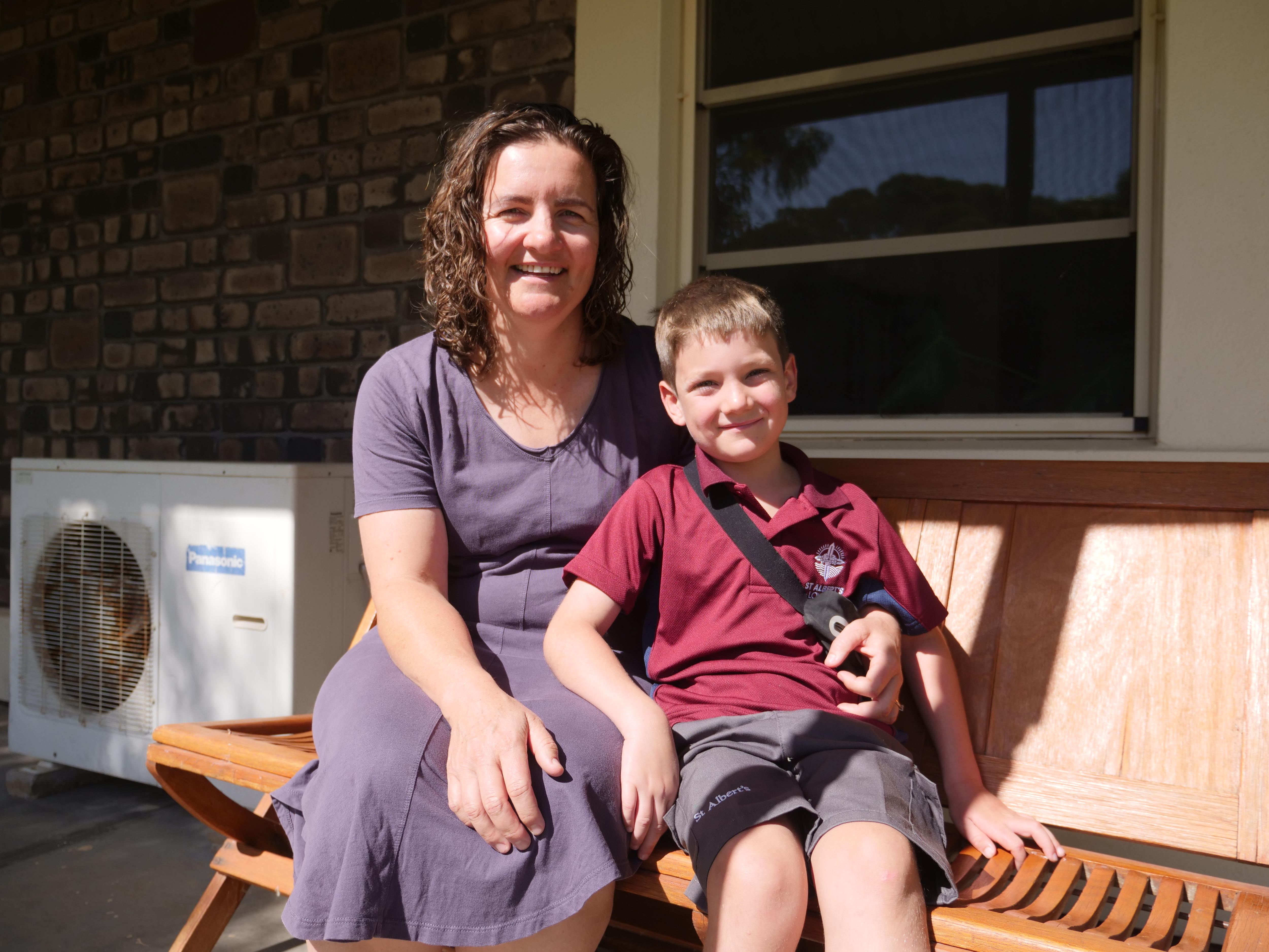 A woman with curly brown hair smiles, her young son has short brown hair and wears a red school uniform