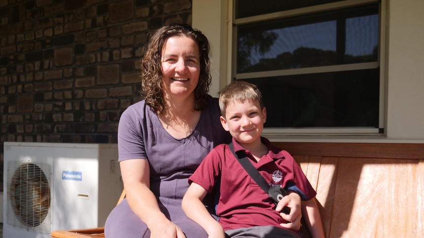 A woman with curly brown hair smiles, her young son has short brown hair and wears a red school uniform